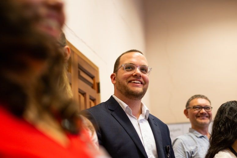 Billedet indeholder sandsynligvis: Menneske, person, jakkesæt, frakke, tøj, overfrakke, tøj, briller, tilbehør, siddende og tilbehør